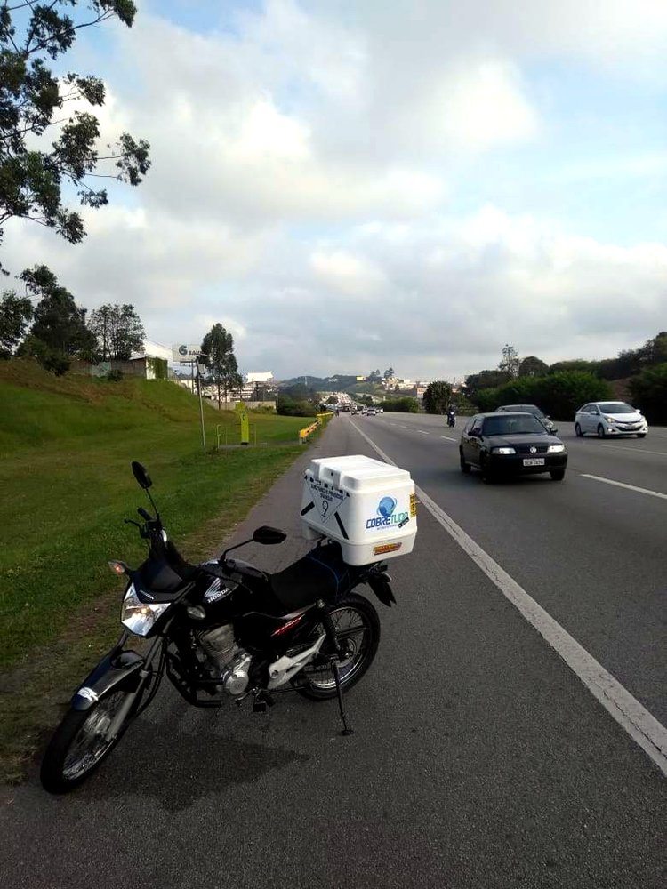 Moto parada no acostamento, baú CobreTudo